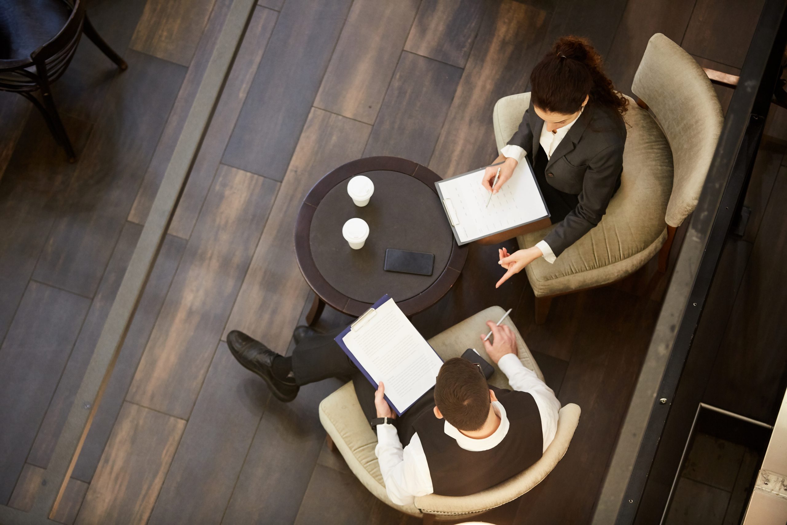 Top view of two young elegant brokers sitting by table and discussing details of contract at working meeting