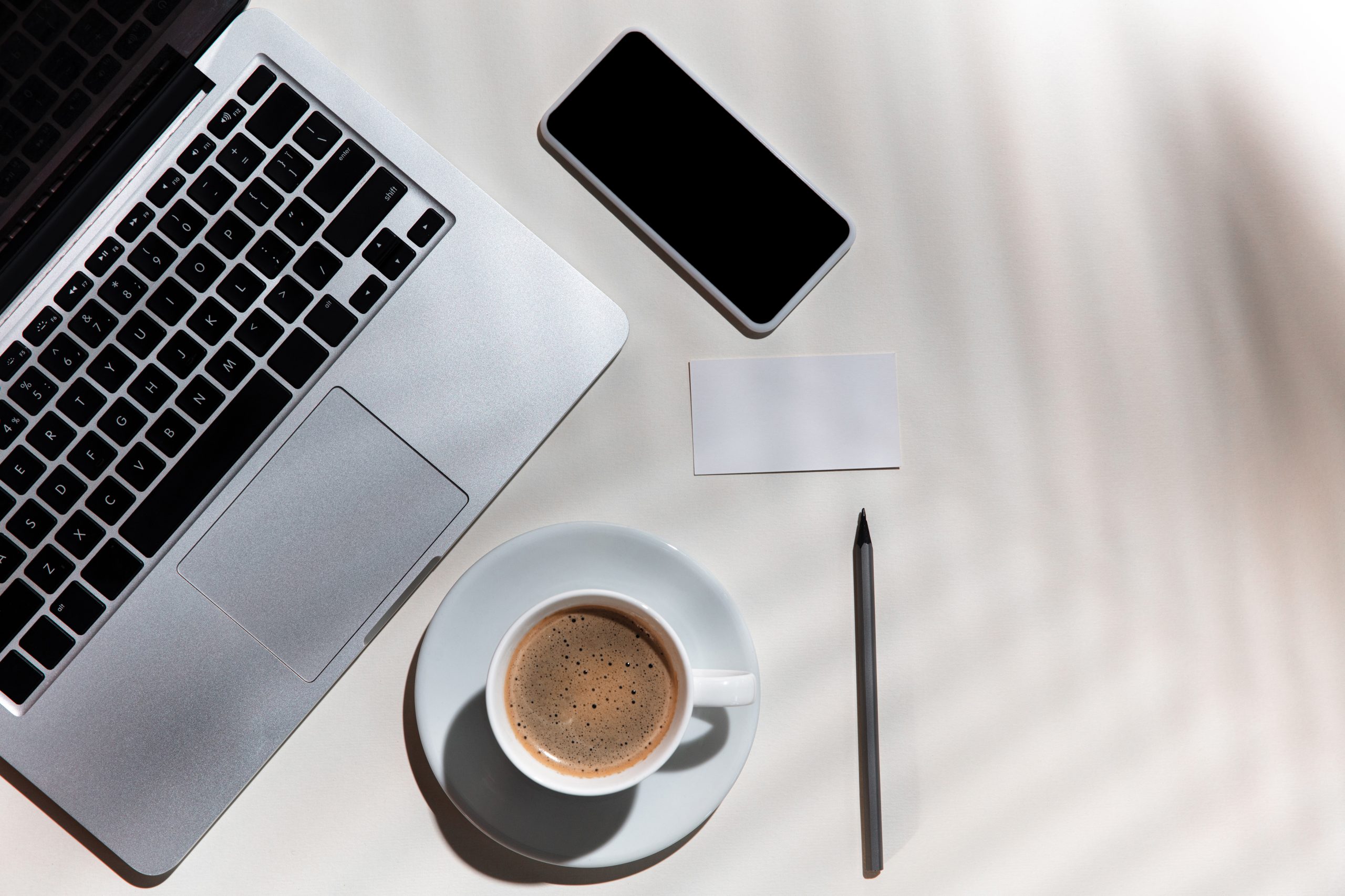 Gadgets, coffee, work tools on a white table indoors. Creative, cozy workplace at home office, inspirational mock up with plant shadows on surface. Concept of remote office, freelance, atmosphere.