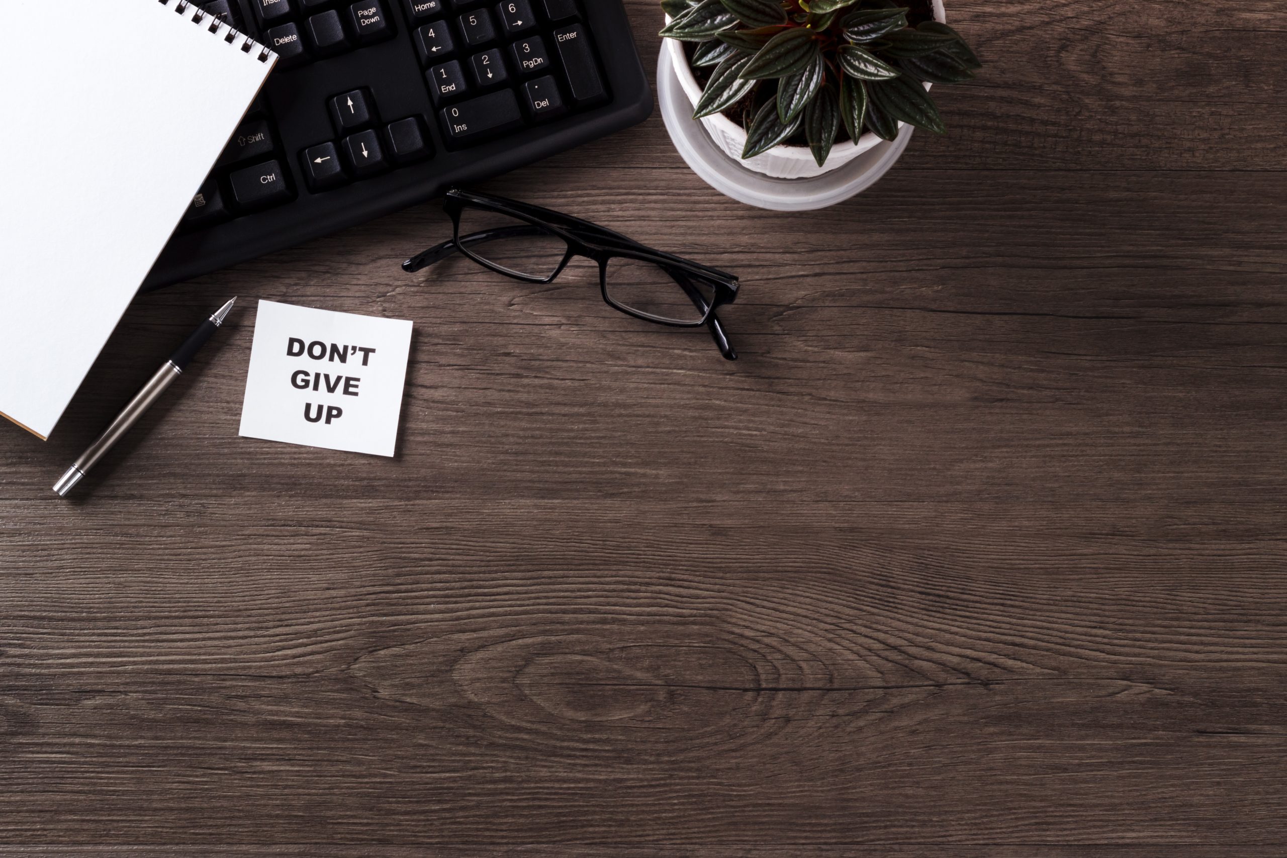 Modern office desk table with keyboard notepad pen plant glasses top view copy space