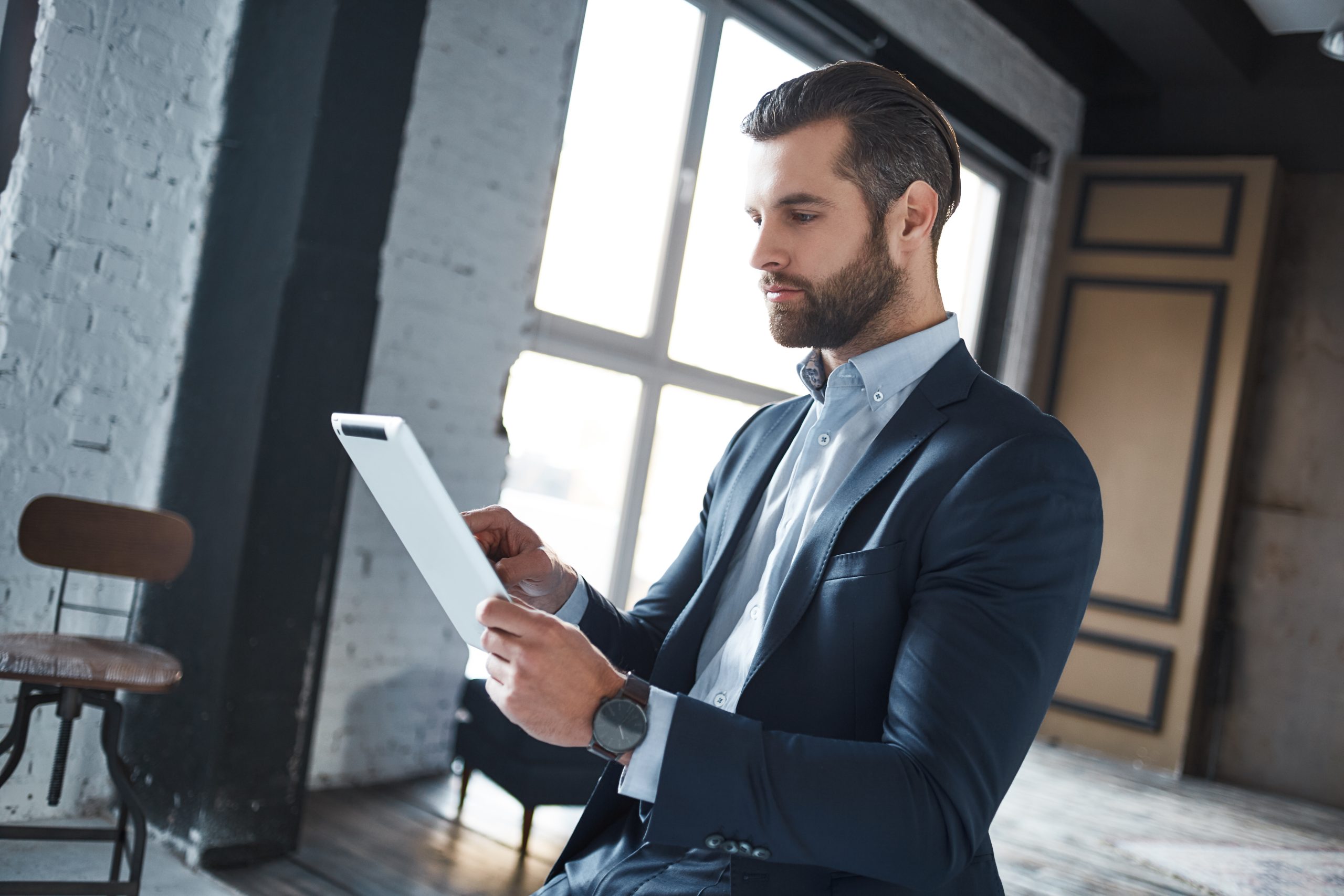 Working hard Confident and young businessman in stylish suit is using his tablet for work. Close-up. Office look.