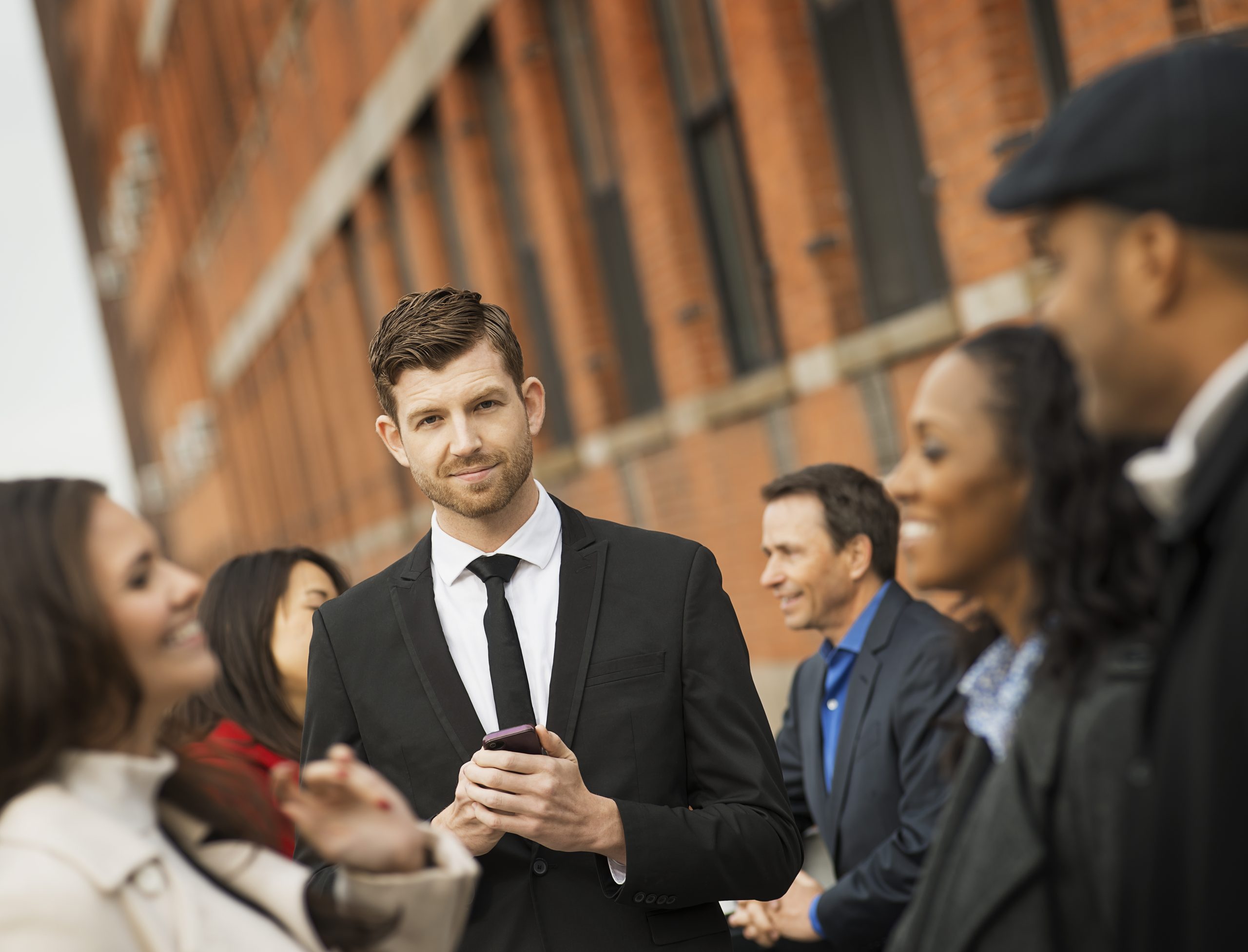 City life. A group of people on the go, keeping in contact, using mobile phones, and talking to each other. Men and women, professionals in a group.