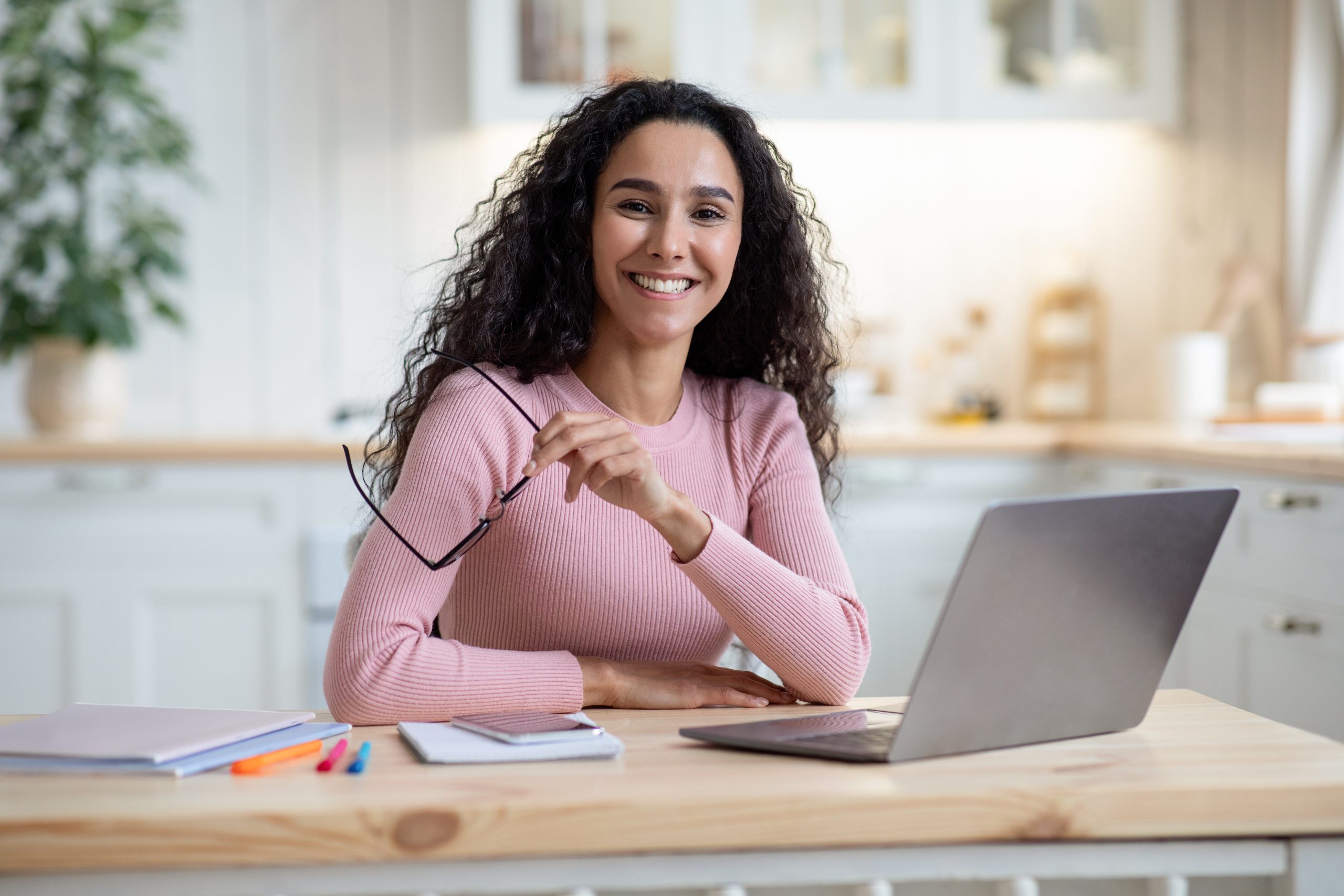 Remote Entrepreneurship. Portrait Of Happy Millennial Woman Sitting At Table With Laptop In Kitchen, Smiling Young Lady Holding Glasses And Looking At Camera, Enjoying Working From Home, Free Space