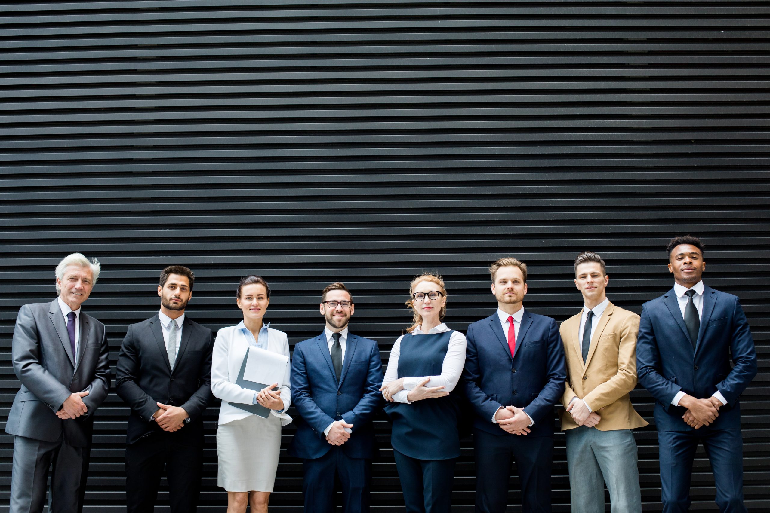 Row of elegant delegates in elegant formalwear standing by dark grey background