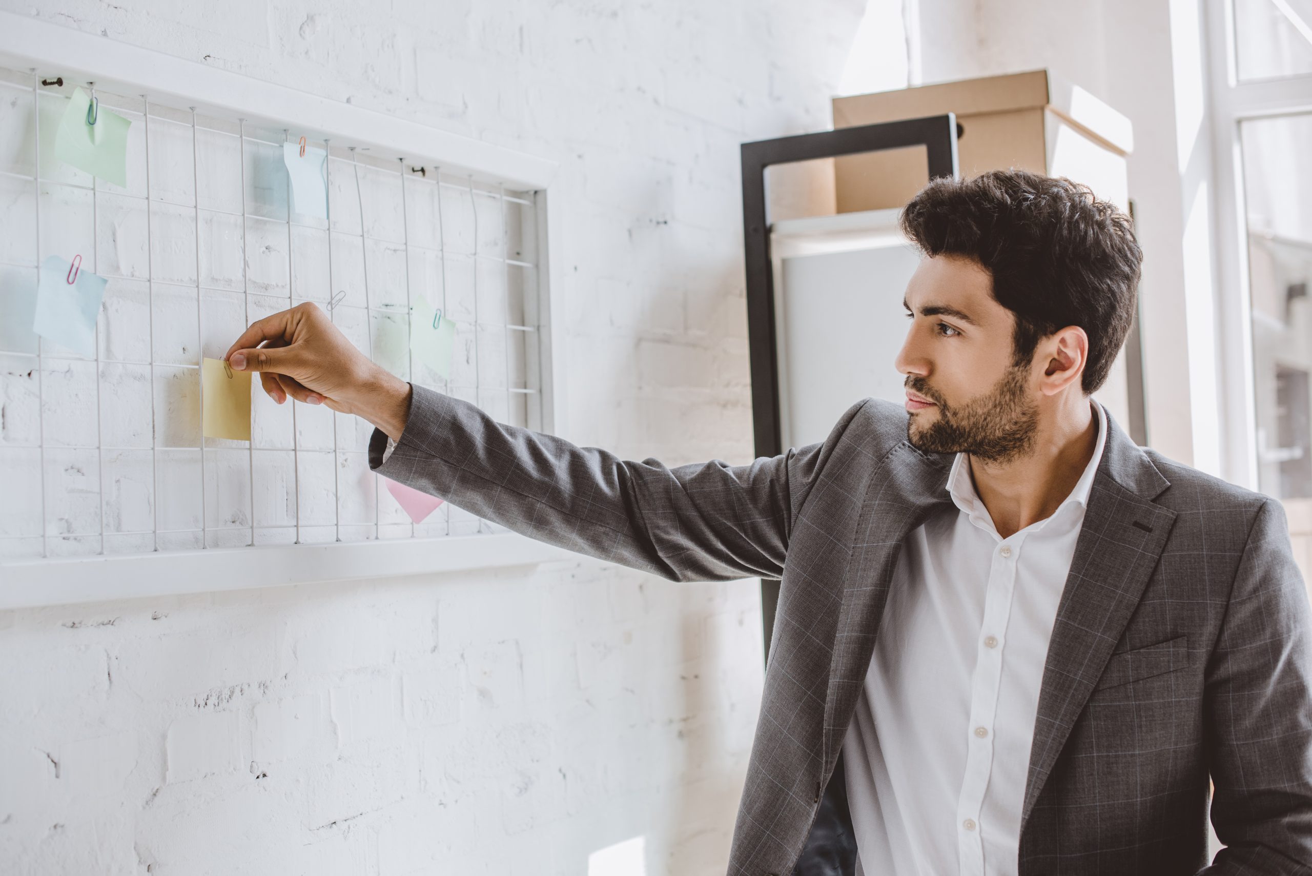 handsome businessman putting paper sticker on task board in office