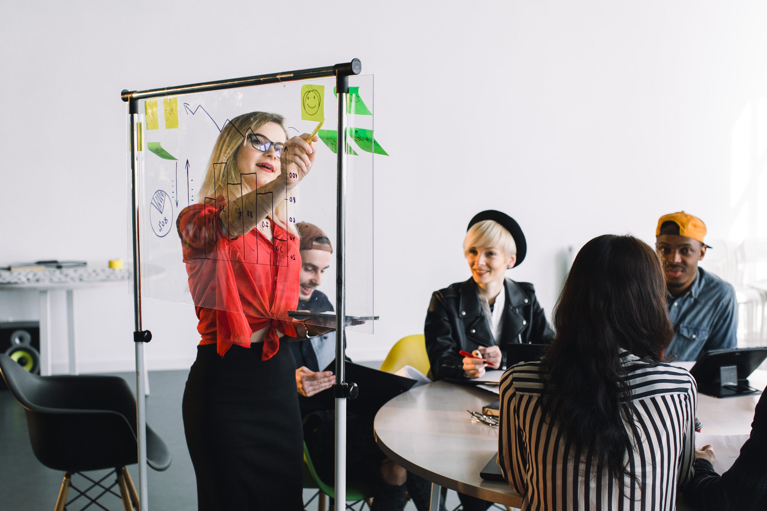 Portrait of young female team leader of talented freelances organizing work of members motivates and inspire them to make researching, standing near glass board in modern coworking space.