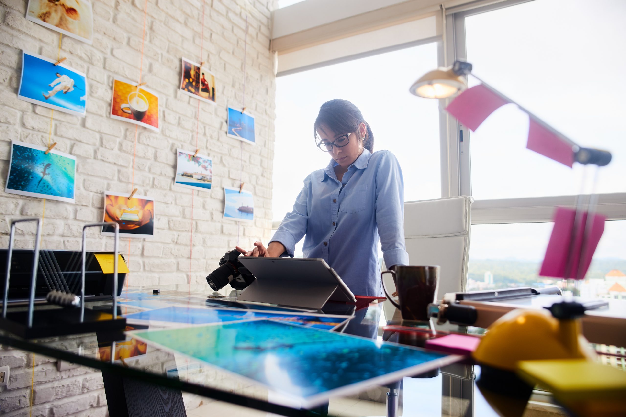 Young people, small business, technology. Woman at work as photographer in office. Hispanic girl using computer laptop for image review, editing.